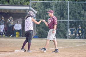 Hannah Langer gets a fist bump from assistant coach Anthony Heronema after making it safely to third base in the home opener against the Thompson Valley Eagles on Aug. 22. John Gardner / The Surveyor