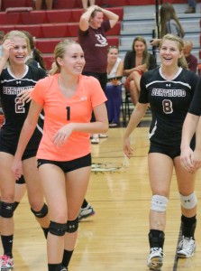 Alyssa Peacock, left, Haley Hummel, center, and Jessa Megenhardt, right, with coach Agho in the background, show their emotions with the win over Erie in 5 sets on Sept. 25. Paula Megenhardt / The Surveyor