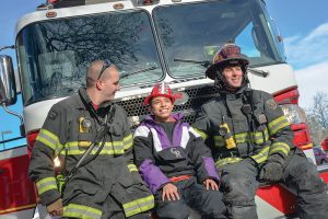 Cisco Debevec sits on the front of the Fire Engine with firefighters Andy Berger, left, and Captain Andrew Kuiken, right. The Surveyor